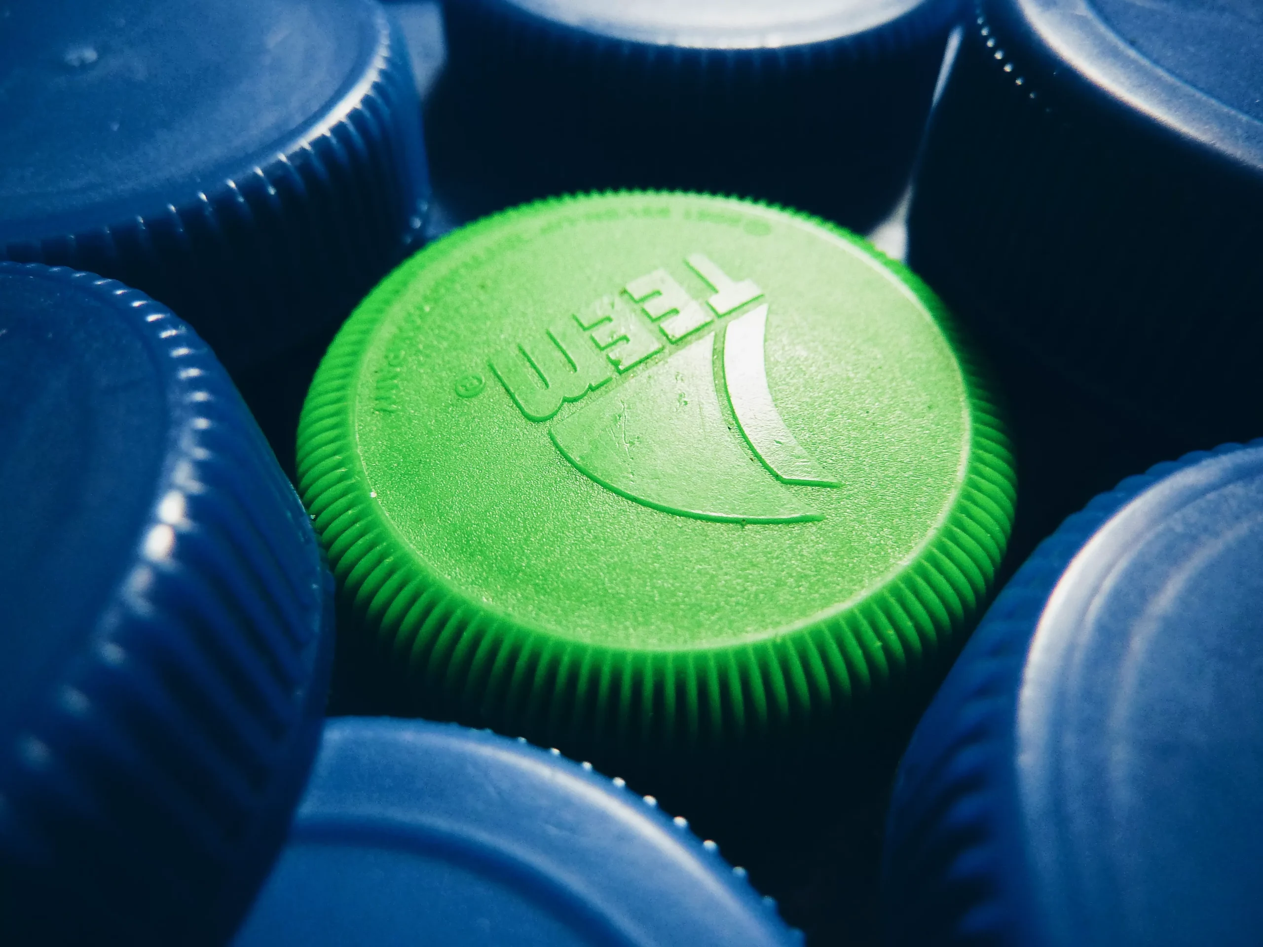 green bottle cap in the center of blue bottle caps